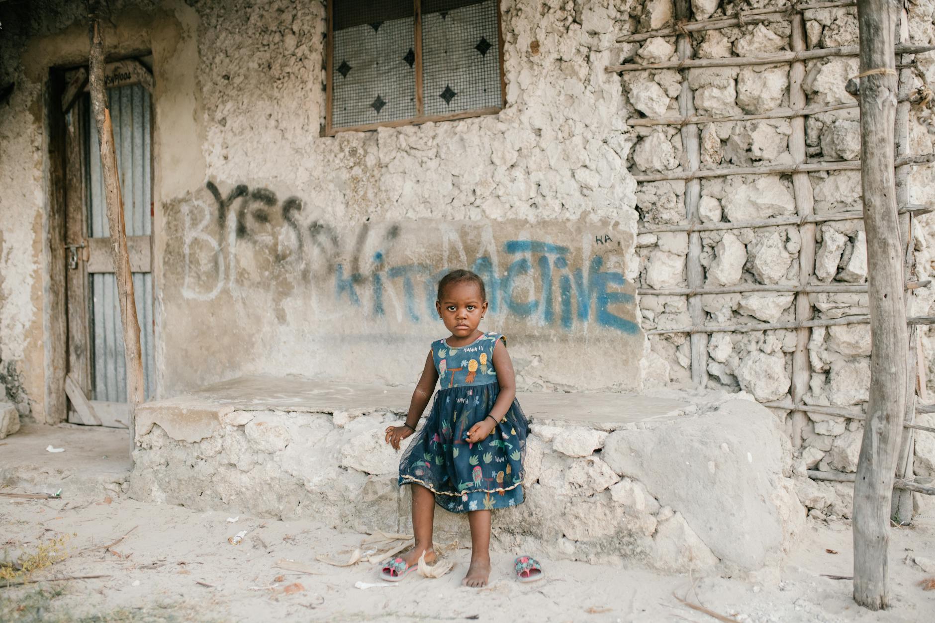 little black girl sitting on rough stone border in ghetto